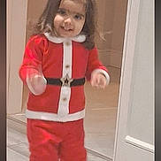 Shanaya Dhingra is registered to the contest to win money with this photo: child, toddler, santa_costume, red_clothing, white_trim, portrait, standing, indoors, doorway, hallway, wood_floor, long_hair, smiling, festive, christmas, boots, costume, full_body, photograph, phone_screenshot