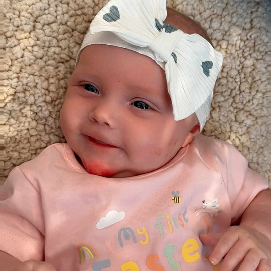 Esme joined the competition — help win amazing prizes! accessories, baby, bodypart, bonnet, cap, clothing, face, finger, hand, happy, hat, head, headband, hood, newborn, person, photography, portrait, quilt, smile
