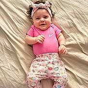 Mackenzie joined the competition — help win amazing prizes! baby, infant, smiling, pink_clothing, headband, bed, blanket, cute, happy, lying_down, patterned_pants, nike_logo, child, indoors, soft_lighting, portrait, one_person, young_child, human, headwear