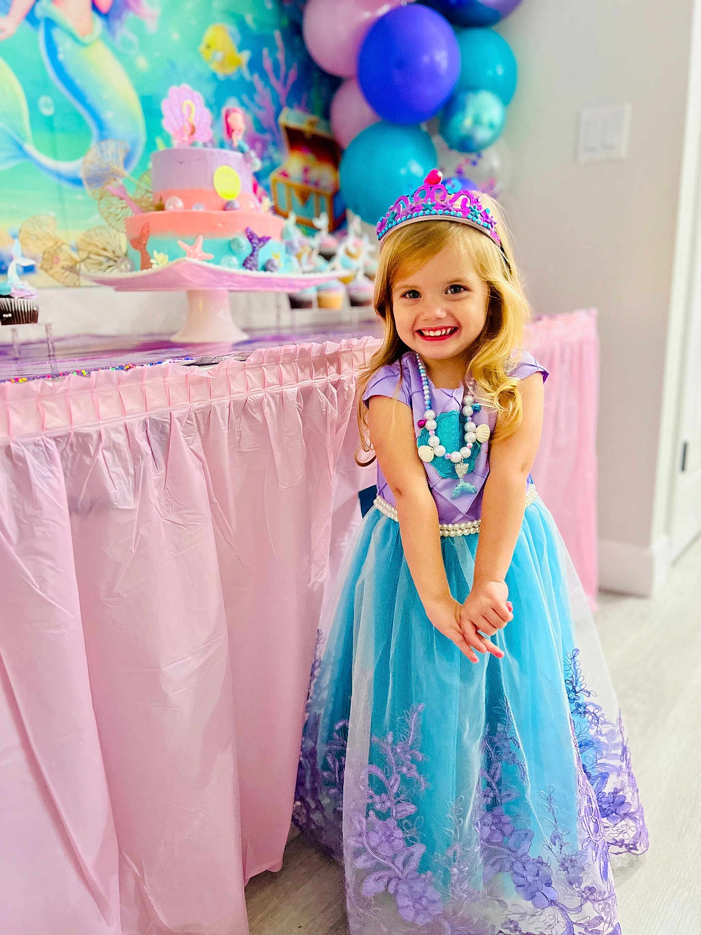Emaleigh is registered to the contest to win money with this photo: child, girl, princess_dress, birthday_party, cake, balloons, smile, party_decoration, table, pastel_colors, necklace, tiara, indoor, celebration, happy, curly_hair, floor, wall, pink, blue