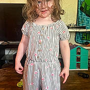 Brighton joined the competition — help win amazing prizes! child, girl, curly_hair, romper, striped_clothing, floral_pattern, smile, indoor, wood_floor, toy_house, television, playful, person, standing, messy_hair, room, head, face, furniture, home