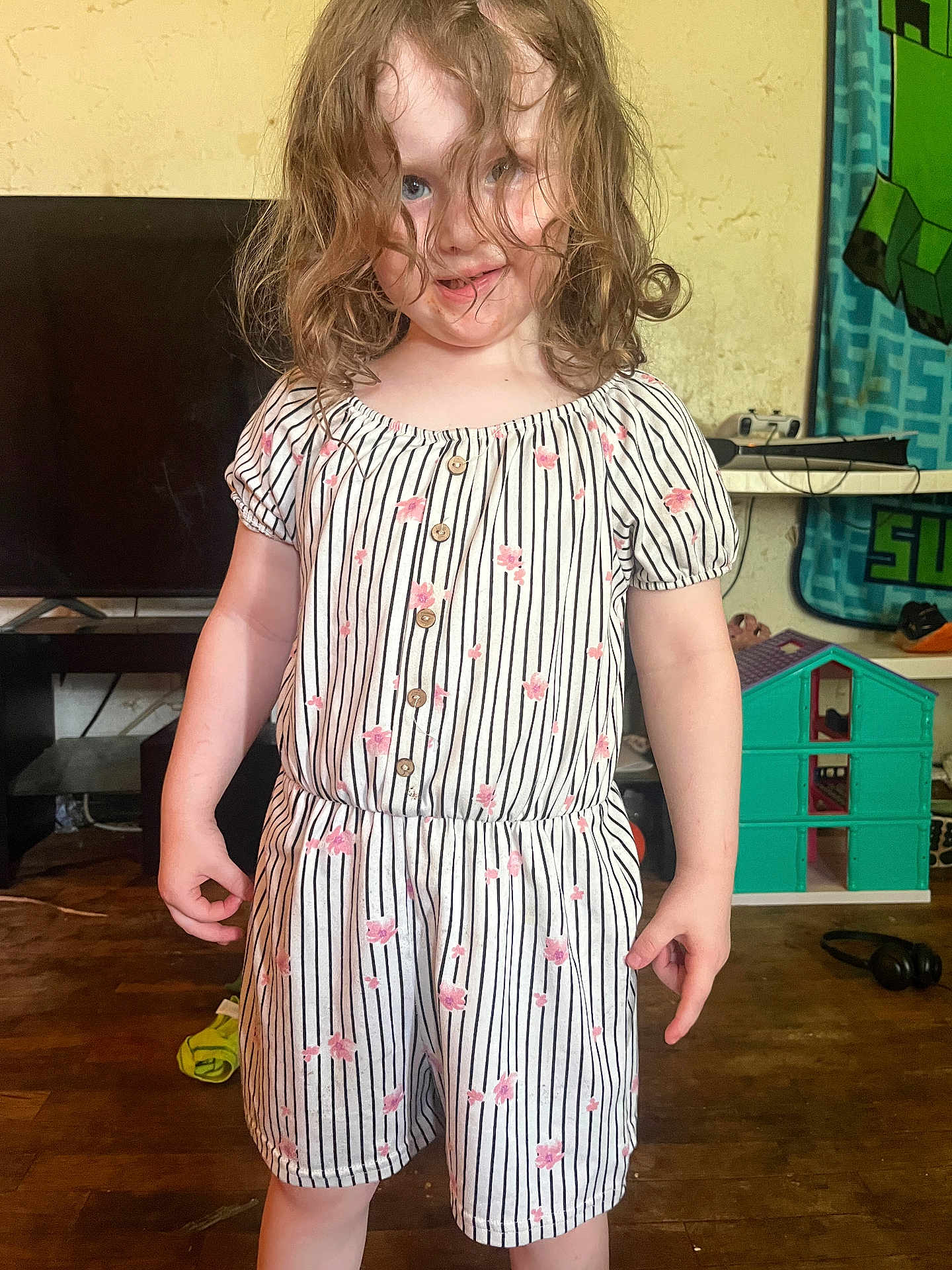 Brighton joined the competition — help win amazing prizes! child, girl, curly_hair, romper, striped_clothing, floral_pattern, smile, indoor, wood_floor, toy_house, television, playful, person, standing, messy_hair, room, head, face, furniture, home