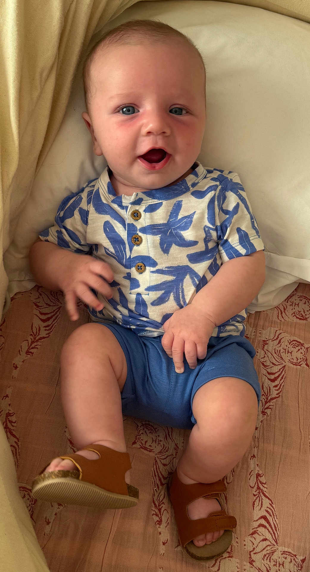 Quinn is registered to the contest to win money with this photo: baby, child, blue_eyes, smiling, sitting, shorts, shirt, sandals, patterned_blanket, indoor, happy, cute, infant, hand, footwear, portrait, casual_clothing, skin, face, expression