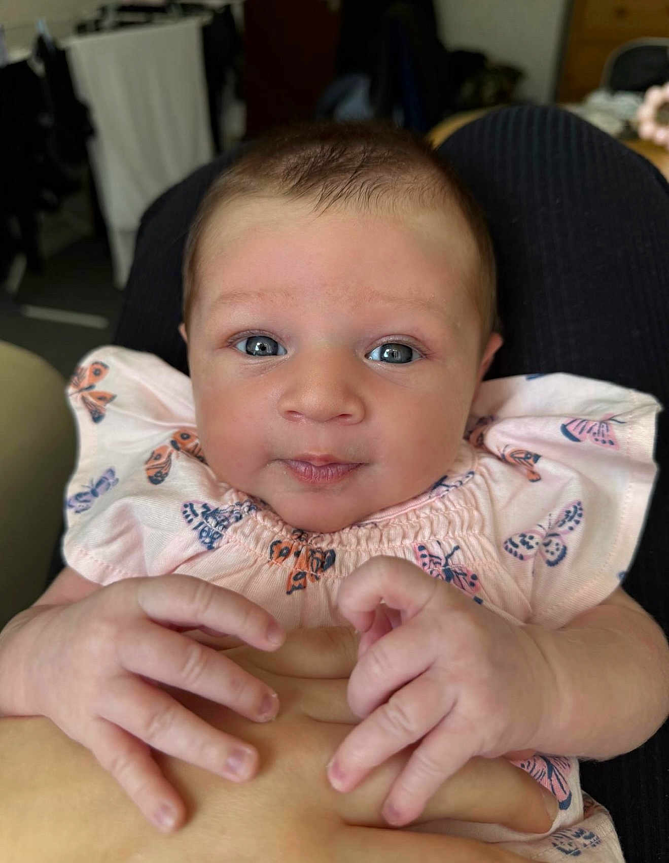Anaya is registered to the contest to win money with this photo: baby, infant, child, hands, face, blue_eyes, pink_clothing, butterfly_pattern, curious_expression, close_up, skin, person, newborn, cute, small_fingers, holding_hand, indoor, soft_light, portrait, human