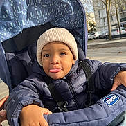Isaac a rejoint le concours — aidez-le/la à gagner de superbes lots ! toddler, child, stroller, jacket, hat, beanie, outdoor, autumn, trees, parked_cars, sunny, face, tongue_out, hand, clothing, person, baby, seatbelt, urban, daylight