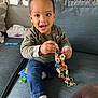 Isaac a rejoint le concours — aidez-le/la à gagner de superbes lots ! toddler, child, smiling, sitting, couch, blue_couch, clothing, toy, colorful, chain, indoor, home, furniture, person, happy, face, jeans, sock, tissue_box, curly_hair