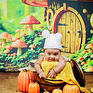 Advik is registered to the contest to win money with this photo: baby, child, pumpkin, hat, bucket, yellow_cloth, mushroom_house, background, autumn, cute, smile, indoors, decorative, orange, wood, playful, festive, portrait, seasonal, fantasy