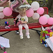 Nova joined the competition — help win amazing prizes! toddler, child, balloons, bench, gifts, outdoor, park, picnic_table, tree, concrete, pink, white, silver_balloon, number_2_balloon, person, shoe, can, gift_bags, clothing, celebration