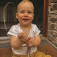 Telio a rejoint le concours — aidez-le/la à gagner de superbes lots ! toddler, child, smiling, sitting, doormat, stone_wall, doorway, pacifier, white_shirt, yellow_pants, twig, indoor, outdoor, happy, cute, baby, portrait, hand, face, eyes