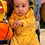 baby, infant, yellow_onesie, giraffe_pattern, plush_toy, blanket, cute, hands_clasped, indoors, portrait, child, soft_toys, colorful, cozy, face, eyes, expression, clothing, lying_down, closeup