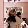 person, cat, mirror, selfie, bedroom, bed, window, ceiling_fan, glasses, phone, pajamas, blanket, furniture, indoor, pet, animal, cute, relaxing, cozy, casual