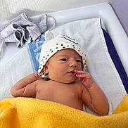 Clémence a rejoint le concours — aidez-le/la à gagner de superbes lots ! baby, newborn, infant, hat, blanket, towel, changing_table, hand, fingers, face, skin, cute, lying_down, nursery, white_towel, yellow_blanket, soft_texture, portrait, cozy, headwear