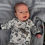 Laney is registered to the contest to win money with this photo: baby, infant, smiling, onesie, animal_print, towel, outdoor, grass, leaves, cute, child, portrait, lying_down, happy, nature, young, casual, cozy, relaxed, playful