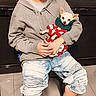 Suavecito joined the competition — help win amazing prizes! baseball_cap, black_wall, casual, chair, clothing, cute, dog, festive_sweater, floor, holding, hoodie, indoor, jeans, person, pet, relaxed, seated, small_dog, smiling, sneakers