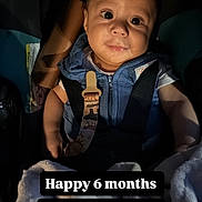 Isaias is registered to the contest to win money with this photo: baby, infant, car_seat, blue_vest, blanket, child, portrait, indoors, seatbelt, cute, smiling, face, person, young_child, sitting, dark_background, soft_light, clothing, happy, celebration