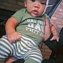 Mckayden is registered to the contest to win money with this photo: baby, child, infant, green_clothing, striped_pants, hand, face, eyes, indoor, brick_wall, person, sitting, cute, expression, sock, holding, portrait, young_child, casual, closeup