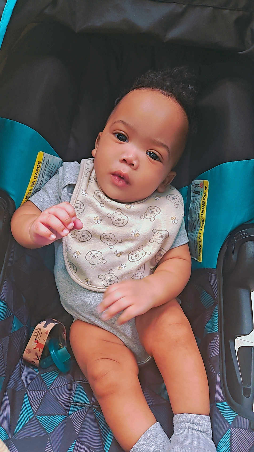 Mckayden is registered to the contest to win money with this photo: baby, child, infant, car_seat, bib, clothing, pattern, pacifier, socks, skin, hand, face, eyes, legs, cute, indoor, seat, fabric, toy, exploring