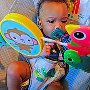 Mckayden is registered to the contest to win money with this photo: baby, baby_seat, bird, child, clothing, colorful, comfort, curly_hair, cute, expression, floor, indoor, infant, monkey, pacifier, play, rainbow, seat, sun, toy