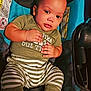 baby, child, car_seat, green_shirt, striped_pants, socks, curly_hair, indoors, cute, infant, young_child, seated, looking, closeup, portrait, fabric, pattern, hands, feet, comfort