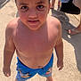 child, boy, curly_hair, barefoot, swim_shorts, blue_shorts, outdoor, sunny, concrete, smiling, summer, playful, standing, casual, happy, person, daylight, skin, young, cute
