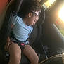 child, car_seat, sleeping, sunlight, window, car_interior, seatbelt, curly_hair, bow, blue_shirt, legs, toddler, young_child, resting, daylight, vehicle, seat, safety, peaceful, cute