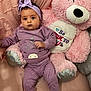 baby, teddy_bear, plush_toy, purple_clothing, headband, infant, cute, soft_toy, pink, smiling_toy, bed, blanket, indoor, child, couch, sitting, portrait, cozy, cute_outfit, young_child