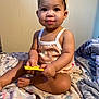 Jordynn is registered to the contest to win money with this photo: toddler, child, baby, headband, romper, floral_pattern, bedspread, blanket, indoor, sitting, holding, curious, smiling, cute, person, skin, hand, foot, young_child, cozy