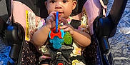 Jordynn is registered to the contest to win money with this photo: baby, child, car_seat, toy, headband, indoor, person, cute, infant, seatbelt, pink, black, socks, legs, face, holding, playful, young, comfort, home