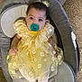 baby, child, pacifier, yellow_dress, daisy_pattern, baby_seat, carpet, infant, cute, comfort, indoors, toddler, sitting, clothing, face, headband, white_tights, looking_at_camera, soft_furniture, relaxed