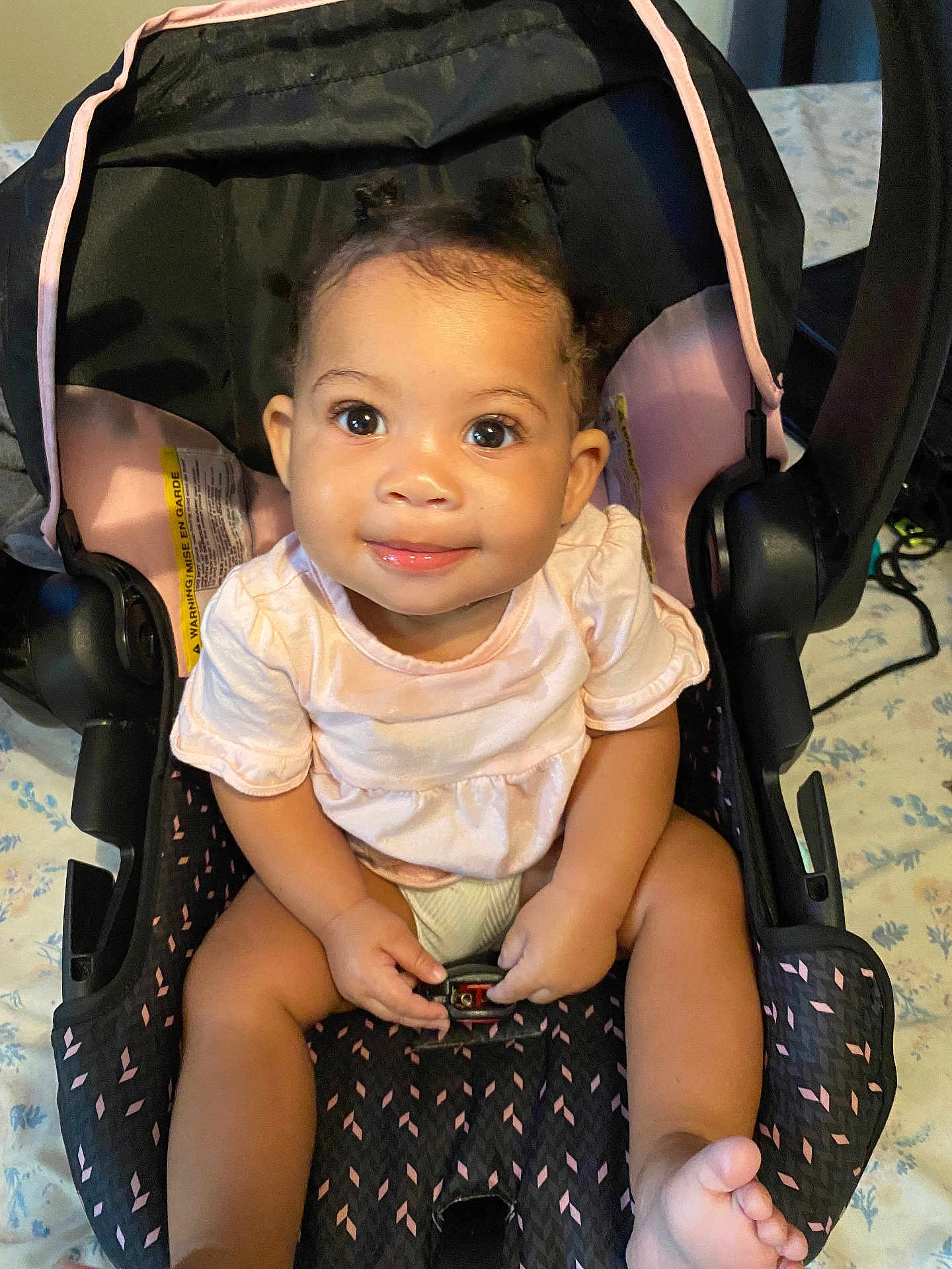 Jordynn is registered to the contest to win money with this photo: baby, child, car_seat, pink_clothing, smile, indoors, seat_belt, infant, cute, happy, person, hair, legs, feet, eyes, face, seat, fabric, pattern, comfort