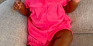 Kalia is registered to the contest to win money with this photo: baby, child, smiling, pink_dress, white_socks, couch, indoor, happy, portrait, infant, person, seated, cute, young_child, furniture, cozy, skin, head, legs, hands