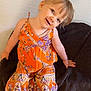 toddler, child, smile, orange_clothing, patterned_clothing, barefoot, blanket, sitting, indoor, wall, happy, cute, young_child, head_tilt, playful, person, portrait, colorful, feet, fabric