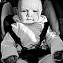 Allie is registered to the contest to win money with this photo: baby, child, car_seat, seatbelt, clothing, hoodie, black_and_white, portrait, infant, face, hand, expression, straps, sitting, young, cute, indoors, cozy, light, shadow