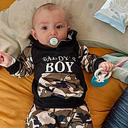 Kayden participe au concours pour gagner de l'argent avec cette photo : baby, child, pacifier, toy, clothing, hoodie, camouflage, bed, pillow, infant, person, lying_down, cute, indoor, soft_toy, young_child, face, hand, sleepwear, comfort