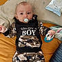 baby, child, pacifier, toy, clothing, hoodie, camouflage, bed, pillow, infant, person, lying_down, cute, indoor, soft_toy, young_child, face, hand, sleepwear, comfort