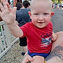 adult_hand, background, casual_clothing, child, daylight, fence, happy, outdoor, park, pavement, people, person, red_shirt, shorts, smiling, summer, tattoo, toddler, trees, waving_hand