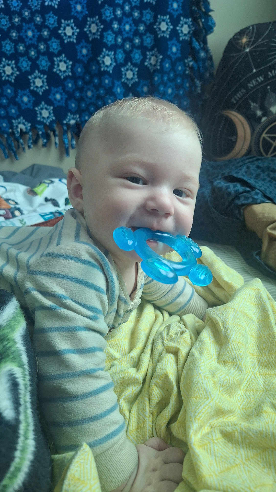 Feilan is registered to the contest to win money with this photo: baby, child, teething_toy, blue, striped_clothing, blanket, bed, indoor, cute, face, smiling, hand, comfort, tapestry, decor, person, portrait, infant, young_child, soft