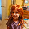 child, girl, smiling, portrait, red_hair, ginger_hair, long_hair, indoor, bedroom, warm_lighting, purple_shirt, standing, face, eyes, nose, mouth, furniture, bed, dresser, photography