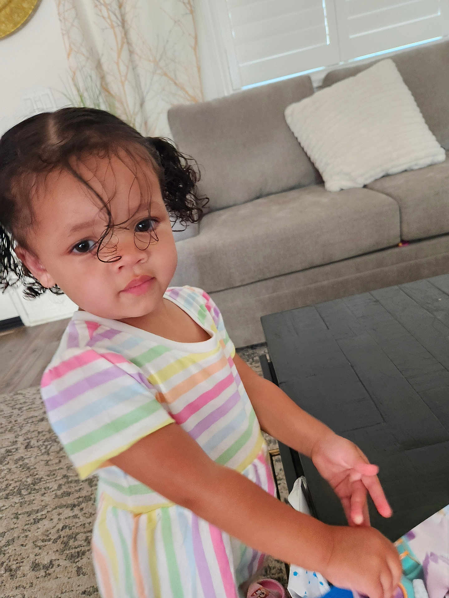 Amilliana joined the competition — help win amazing prizes! toddler, child, curly_hair, pigtails, striped_dress, indoor, living_room, table, couch, carpet, face, person, cute, young_child, hair, furniture, home_decor, plant, colorful_clothing, portrait