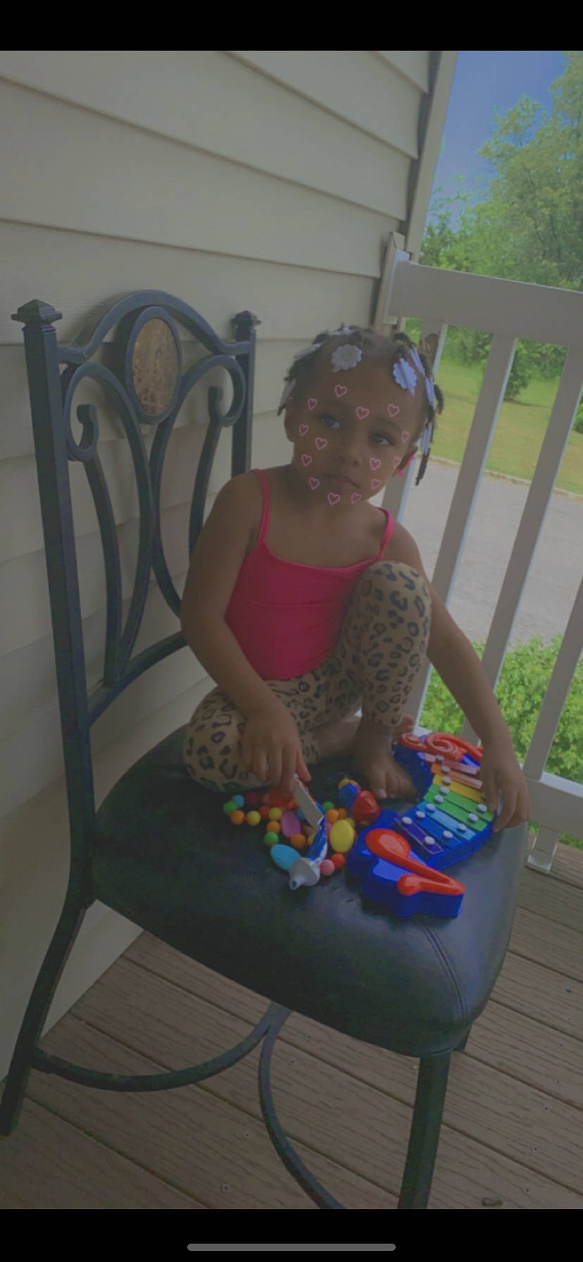 Jada is registered to the contest to win money with this photo: baby_toddler_clothing, chair, child, comfort, fence, flooring, fun, human_leg, lap, leisure, outdoor_furniture, person, plant, recreation, room, sitting, smile, thigh, toddler, toy