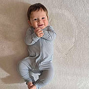 James joined the competition — help win amazing prizes! baby, infant, child, onesie, smile, hands, feet, lying_down, blue_clothing, soft_texture, face, happy, cute, portrait, human, young_child, indoors, skin, head, expression