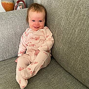Lily joined the competition — help win amazing prizes! baby, infant, smiling, onesie, pink_clothing, couch, gray_furniture, living_room, portrait, happy, child, indoor, seated, cozy, decor, vase, photo_frame, home, cute, relaxed