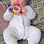 baby, child, infant, onesie, toy, teething_toy, couch, cushion, smiling, happy, sitting, indoor, cute, face, hand, foot, fabric, comfort, playful, relaxed