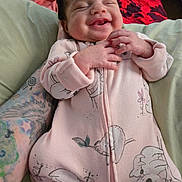 Soliana is registered to the contest to win money with this photo: animal_print, baby, bed, blanket, child, cozy, cute, hand, happy, indoor, infant, onesie, person, pink_clothing, portrait, relaxed, sleepy_eyes, smiling, soft, tattoo