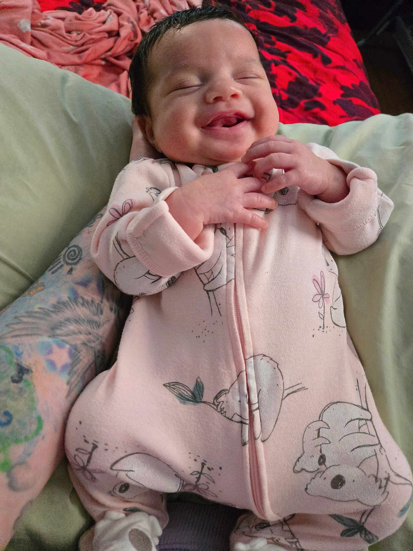 Soliana is registered to the contest to win money with this photo: animal_print, baby, bed, blanket, child, cozy, cute, hand, happy, indoor, infant, onesie, person, pink_clothing, portrait, relaxed, sleepy_eyes, smiling, soft, tattoo