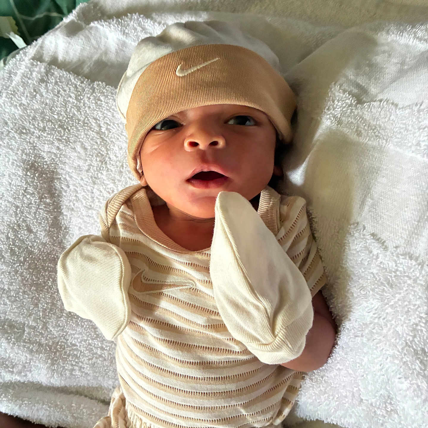 Acaio is registered to the contest to win money with this photo: baby, newborn, infant, mittens, hat, beige_clothing, towel, lying_down, face, open_mouth, curious, soft_texture, fabric, closeup, person, cute, small, resting, indoors, cozy