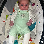 Freya is registered to the contest to win money with this photo: baby, infant, child, romper, white_tights, baby_rocker, colorful, wide_eyes, knitted_clothing, seated, indoors, expression, cute, small_hands, soft_fabric, patterned_background, newborn, clothing_buttons, baby_garment, portrait
