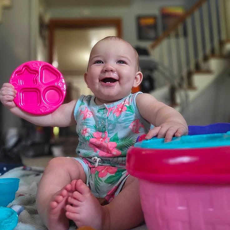 Maeve is registered to the contest to win money with this photo: baby, blanket, child, colorful, cute, face, feet, fun, happy, house, indoors, infant, person, plastic, play, romper, sitting, smiling, staircase, toy
