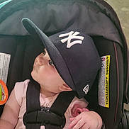 Maeve joined the competition — help win amazing prizes! baby, black_cap, cap, car_seat, child, closeup, cute, face, hand, hat, indoor, infant, looking, person, pink_clothing, seatbelt, sitting, straps, warning_label, young
