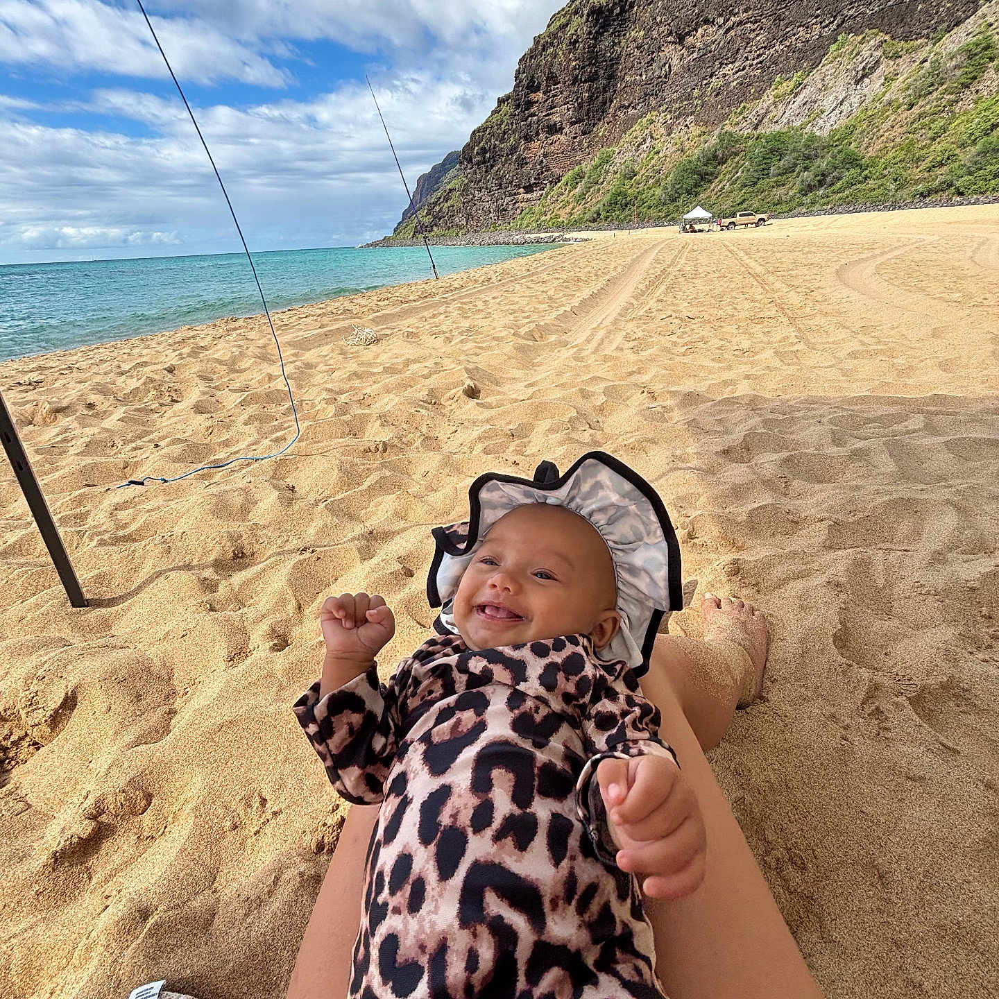 Mailehea is registered to the contest to win money with this photo: baby, beach, cliffs, clouds, happy, hat, infant, legs, leopard_print, nature, ocean, outdoor, relaxing, sand, sky, smiling, sunshine, towel, vacation, water